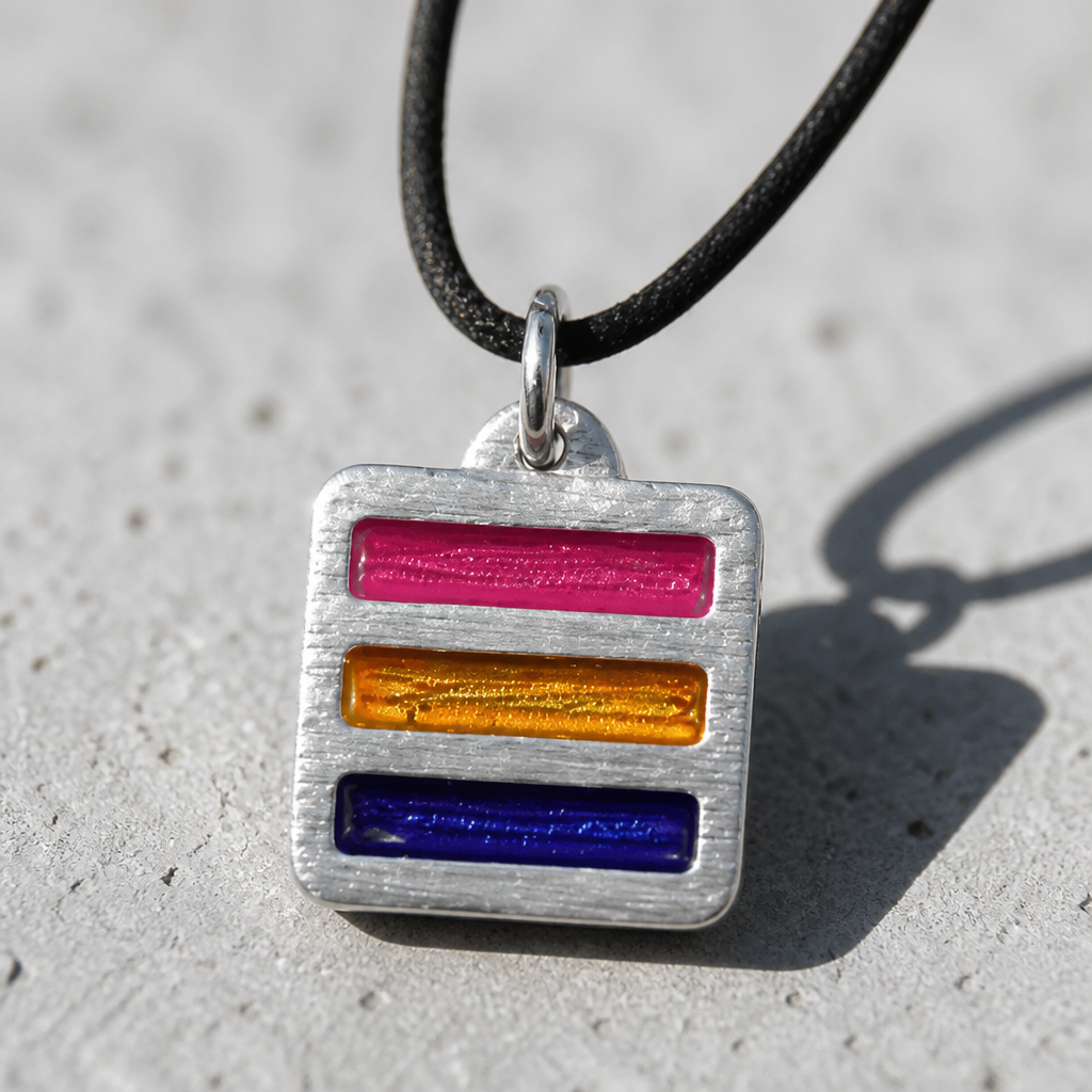 Handcrafted pewter pendant featuring the Pansexual Pride flag in a contemporary geometric design on an adjustable black waxed cord on a concrete surface