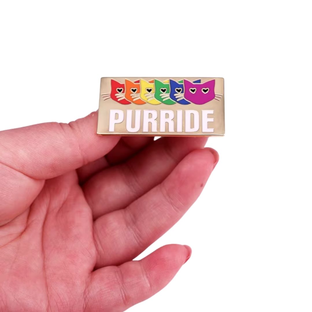 hand holding Purride enamel pin featuring six rainbow-colored cats and Pride-inspired design