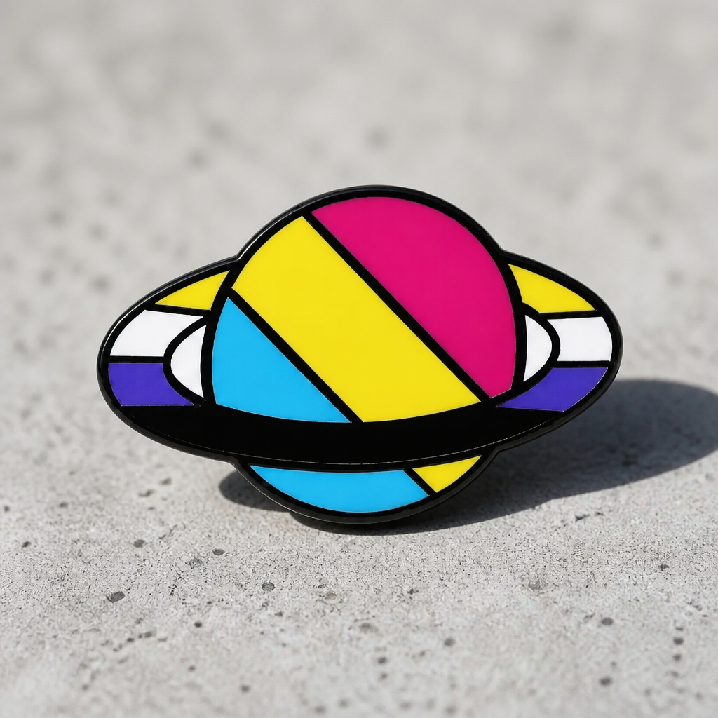 Saturn-inspired enamel pin featuring Pansexual and Nonbinary Pride flag colors on a ringed planet design on a concrete surface