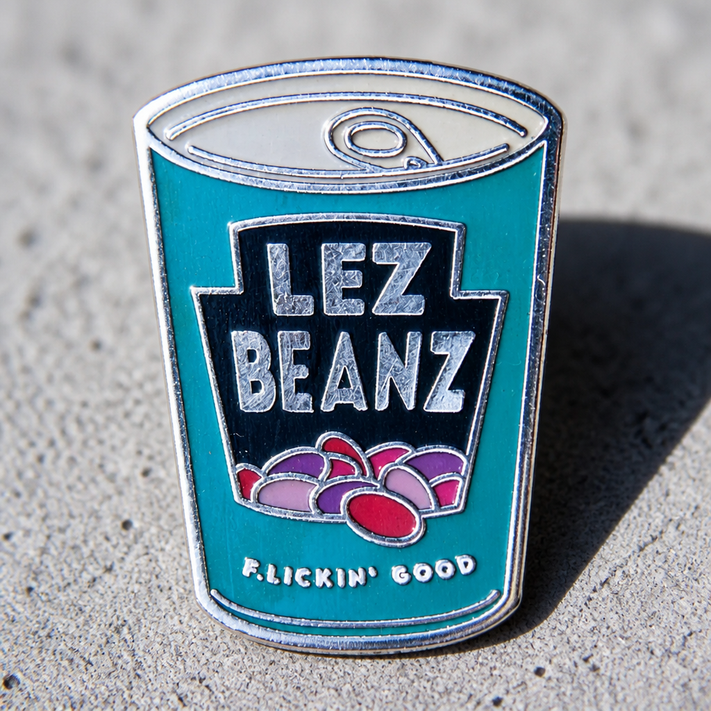 Lez Beanz enamel pin featuring a retro-style can of beans with playful lesbian pride humor on a concrete surface