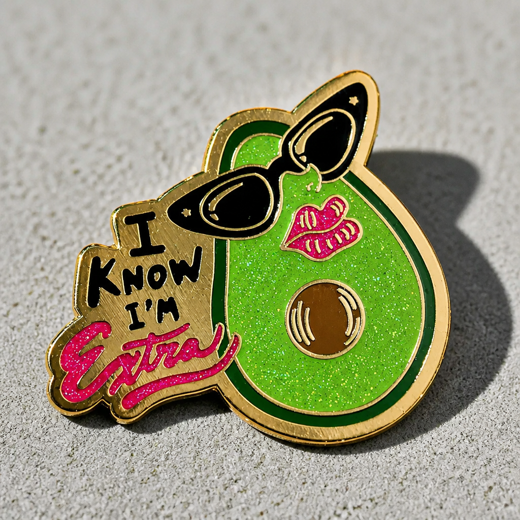 Glitter avocado enamel pin wearing sunglasses with the phrase I Know I'm Extra on a concrete surface