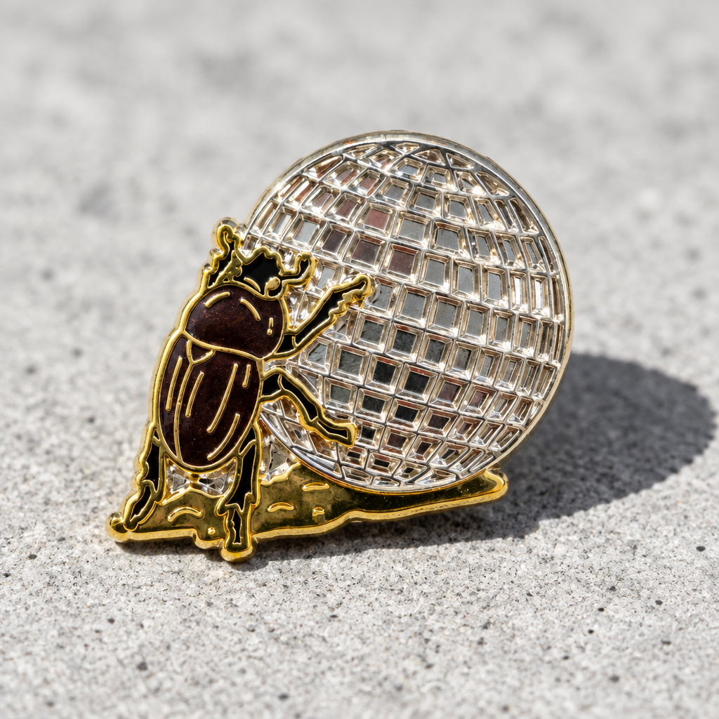 Disco Beetle enamel pin featuring a brown beetle rolling a large silver disco ball on a concrete surface
