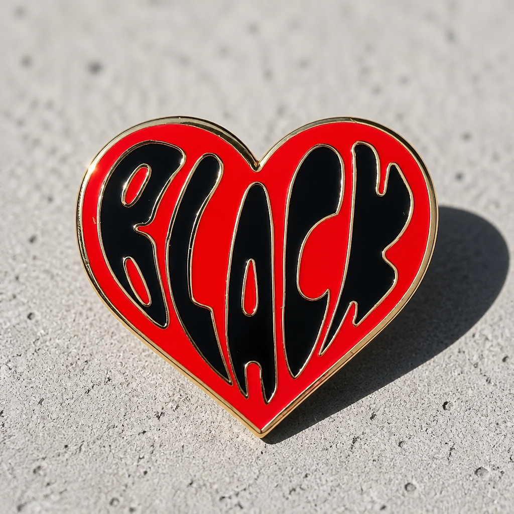 Black Love heart-shaped hard enamel pin by Rebellious Pins with shiny gold plating and bold red lettering celebrating Black love and community displayed on a concrete surface