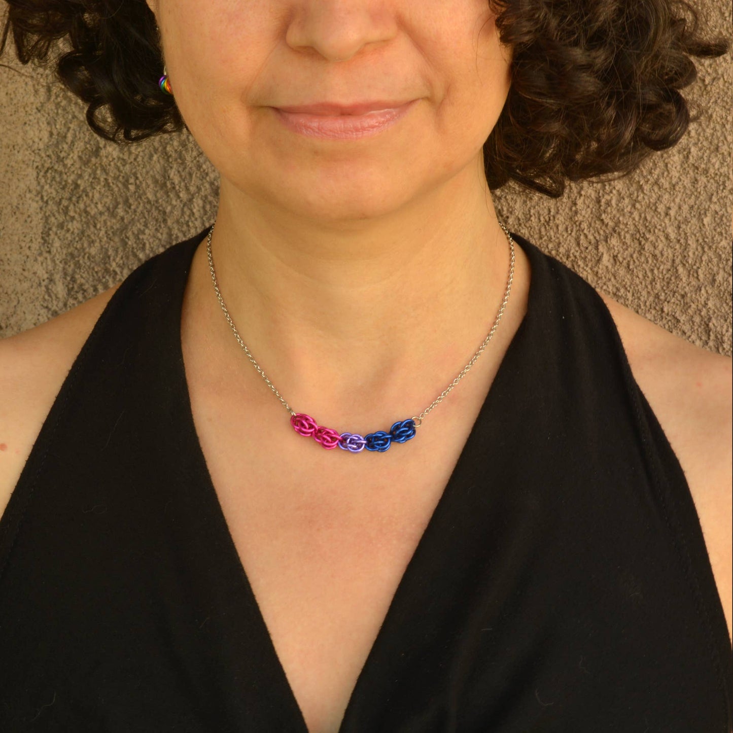 a close-up of a person wearing a Hand-linked bisexual pride chainmail necklace featuring pink, purple, and blue aluminum rings on an adjustable stainless steel chain.