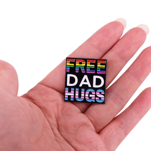 Free Dad Hugs enamel pin with Progress Pride rainbow colors on black background held in a hand