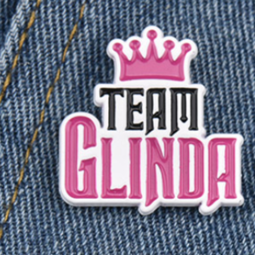 Pink Team Glinda musical theater fandom pin with crown detail on denim background