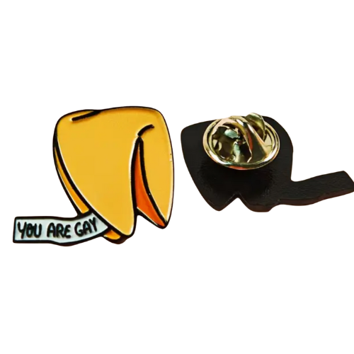 Golden fortune cookie enamel pin with tiny “You Are Gay” fortune message