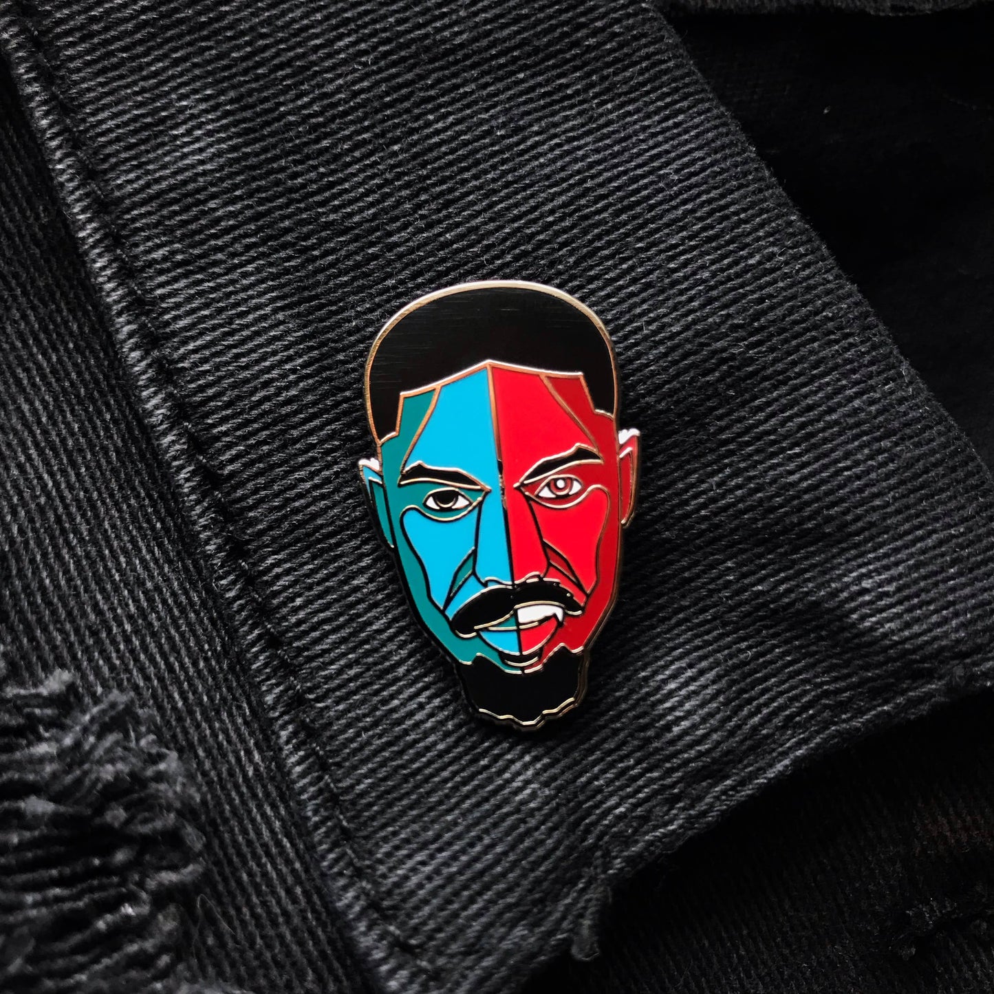 Hard enamel pin featuring a stylized portrait inspired by Smoke from the film Sinners with bold red and blue artwork and silver-plated details on a black denim jacket