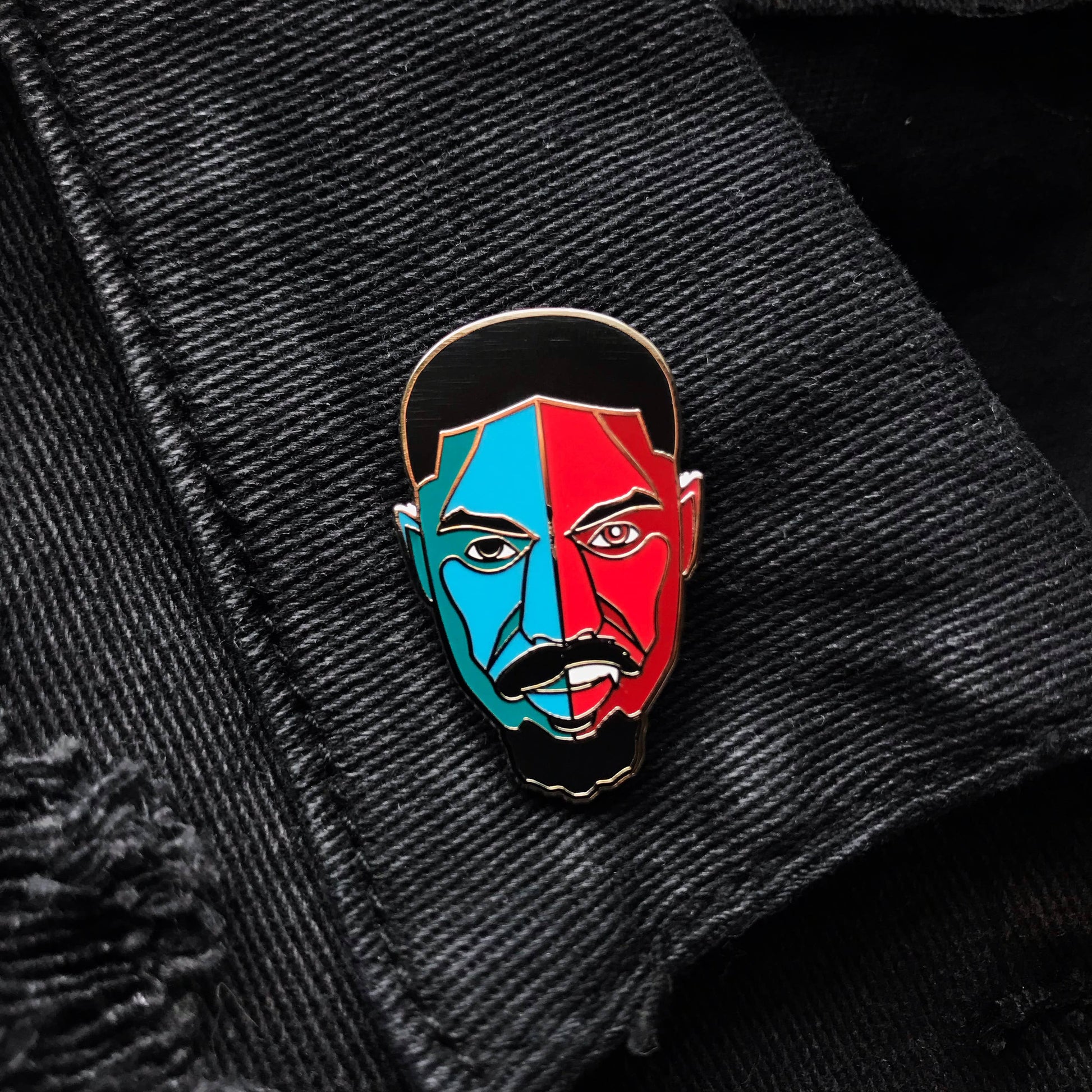 Hard enamel pin featuring a stylized portrait inspired by Smoke from the film Sinners with bold red and blue artwork and silver-plated details on a black denim jacket
