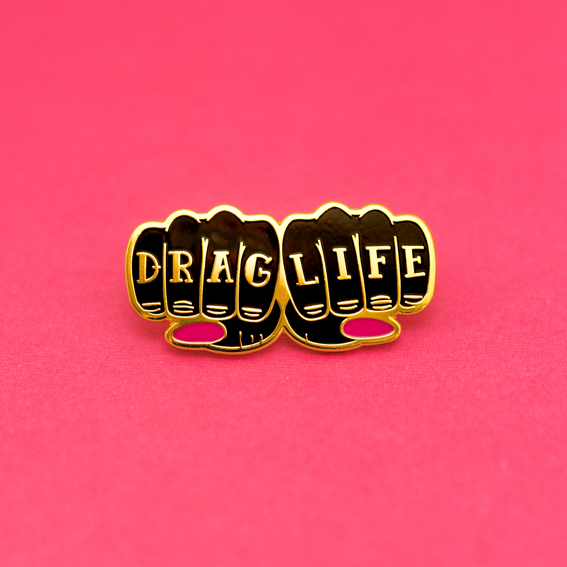Drag Life enamel pin featuring gold-tone knuckle lettering with pink accent details on a pink background.