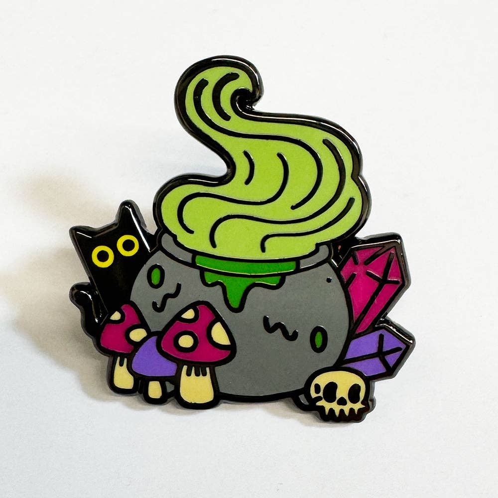Witchy Cauldron enamel pin featuring a bubbling green cauldron, black cat, crystals, mushrooms, and skull details