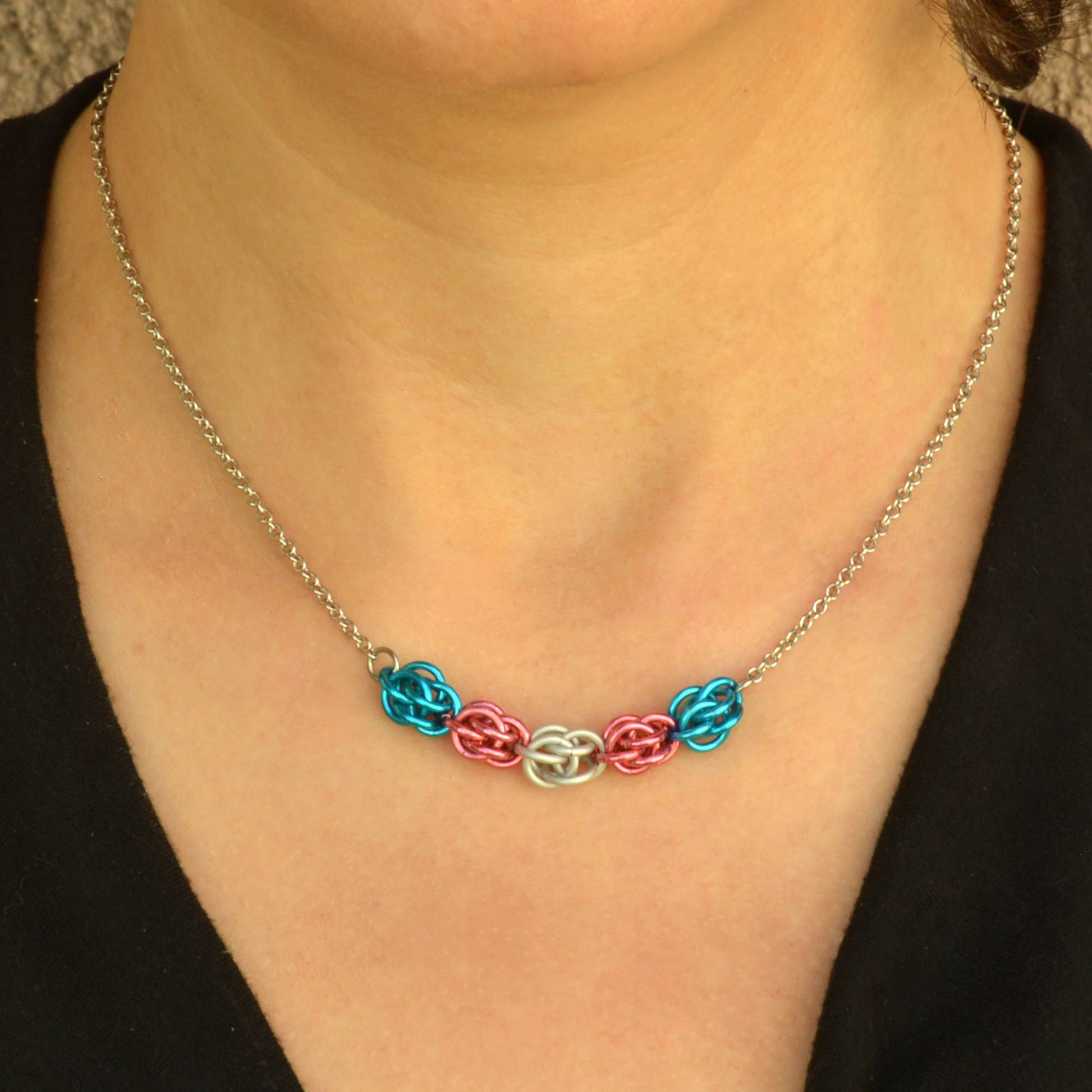 a close-up of a person wearing a Hand-linked transgender pride chainmail necklace featuring blue, pink, and white aluminum rings on an adjustable stainless steel chain.