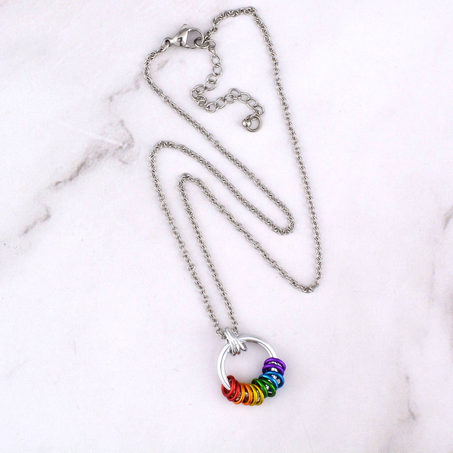 Handcrafted LGBTQ+ rainbow minimalist coil fidget necklace featuring twelve free-spinning aluminum rings on an adjustable stainless steel chain displayed on a marble surface