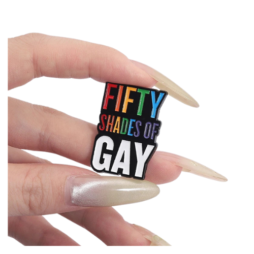 Rainbow enamel pin reading “Fifty Shades of Gay” held between fingers