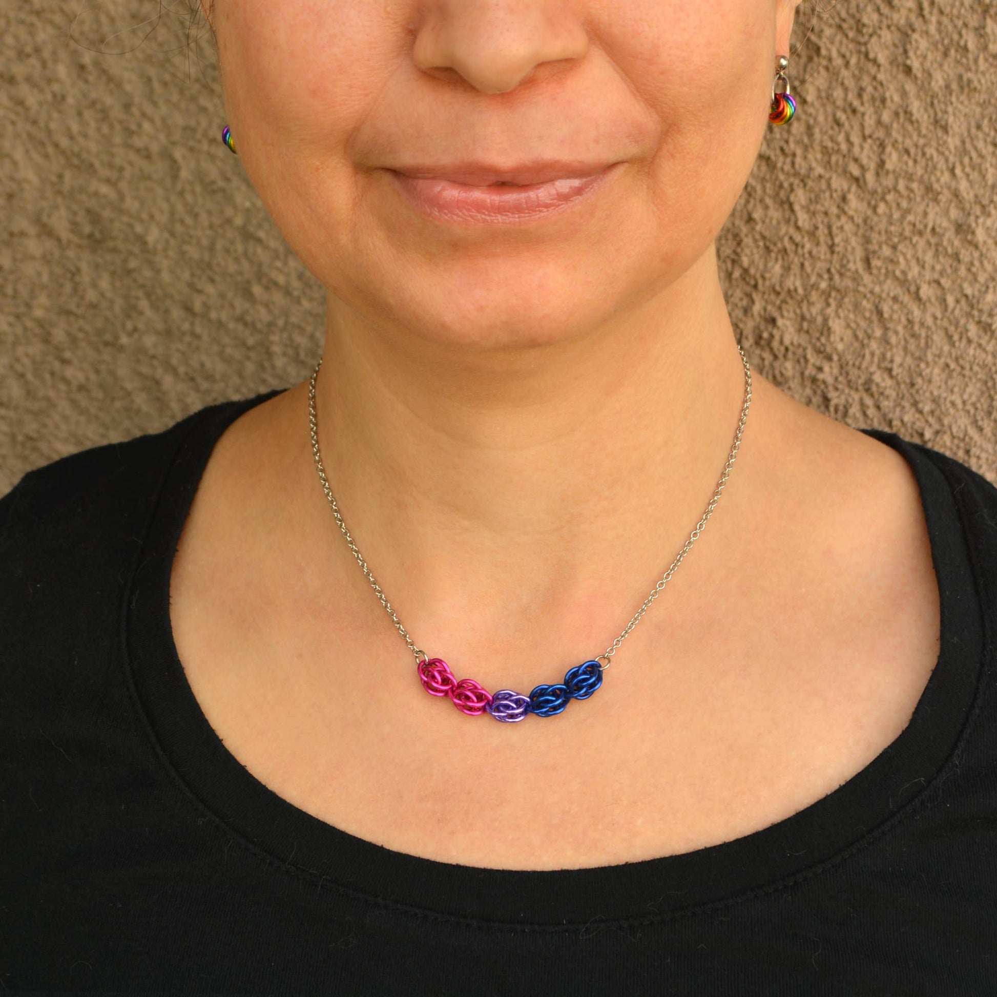a close-up of a person wearing a Hand-linked bisexual pride chainmail necklace featuring pink, purple, and blue aluminum rings on an adjustable stainless steel chain.