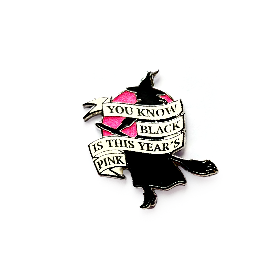Glitter enamel pin featuring a witch silhouette flying across a pink moon with the phrase Black Is This Year’s Pink