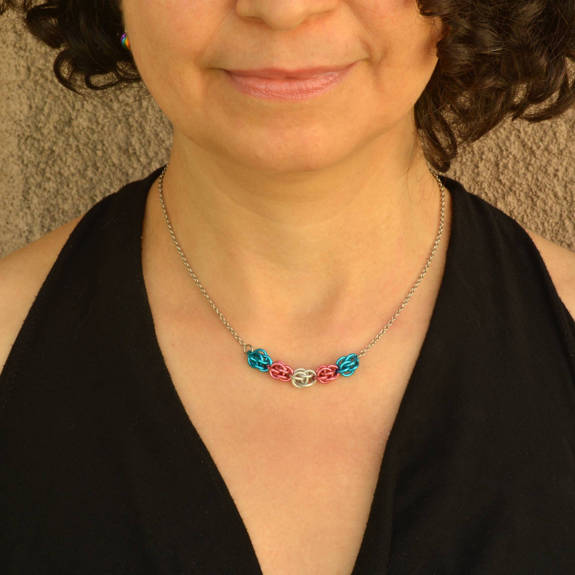 a close-up of a woman wearing a Hand-linked transgender pride chainmail necklace featuring blue, pink, and white aluminum rings on an adjustable stainless steel chain.