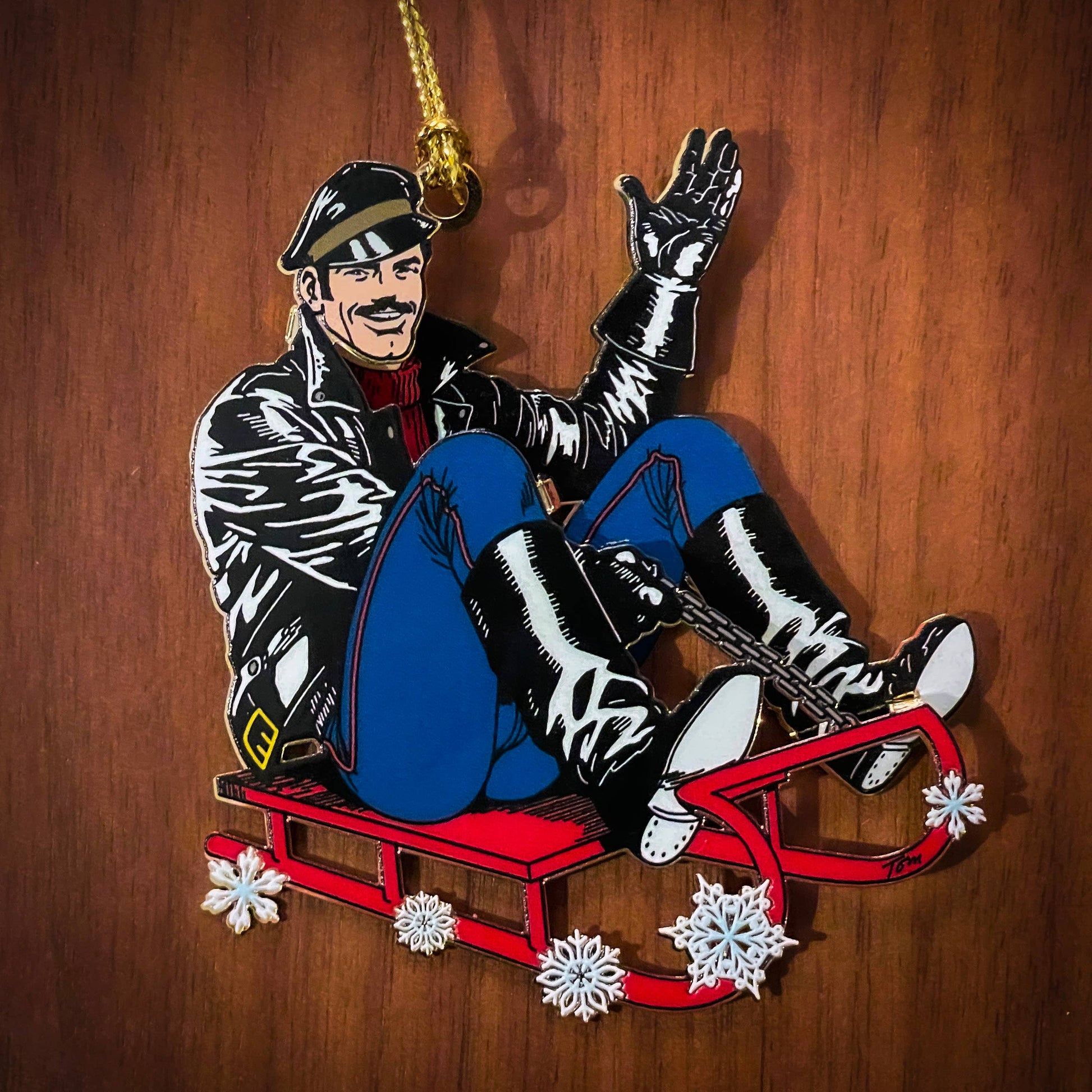 Limited edition Tom of Finland leather sled metal ornament featuring a leather-clad character riding a red sled
