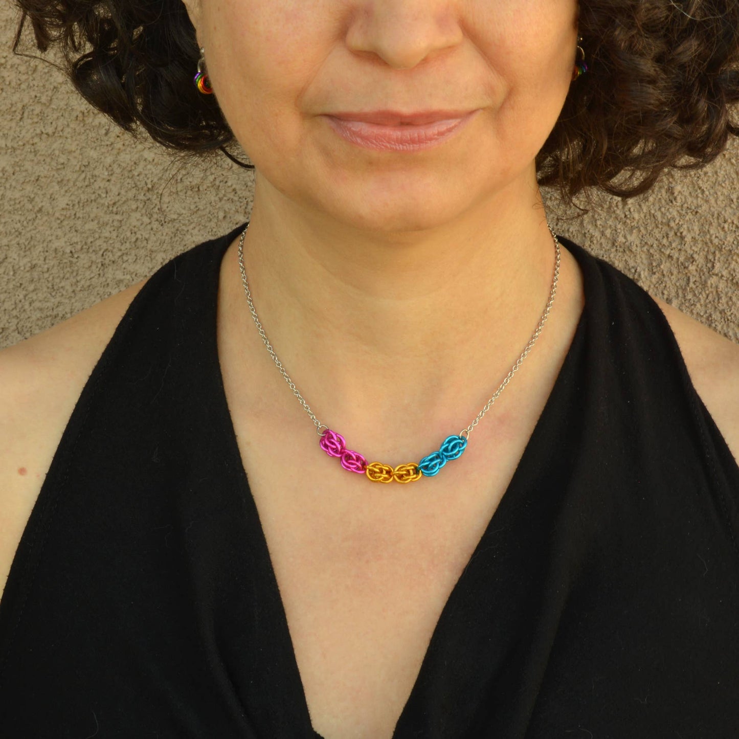 a close-up of a woman wearing a Hand-linked pansexual pride chainmail necklace featuring pink, yellow, and blue aluminum rings on an adjustable stainless steel chain.