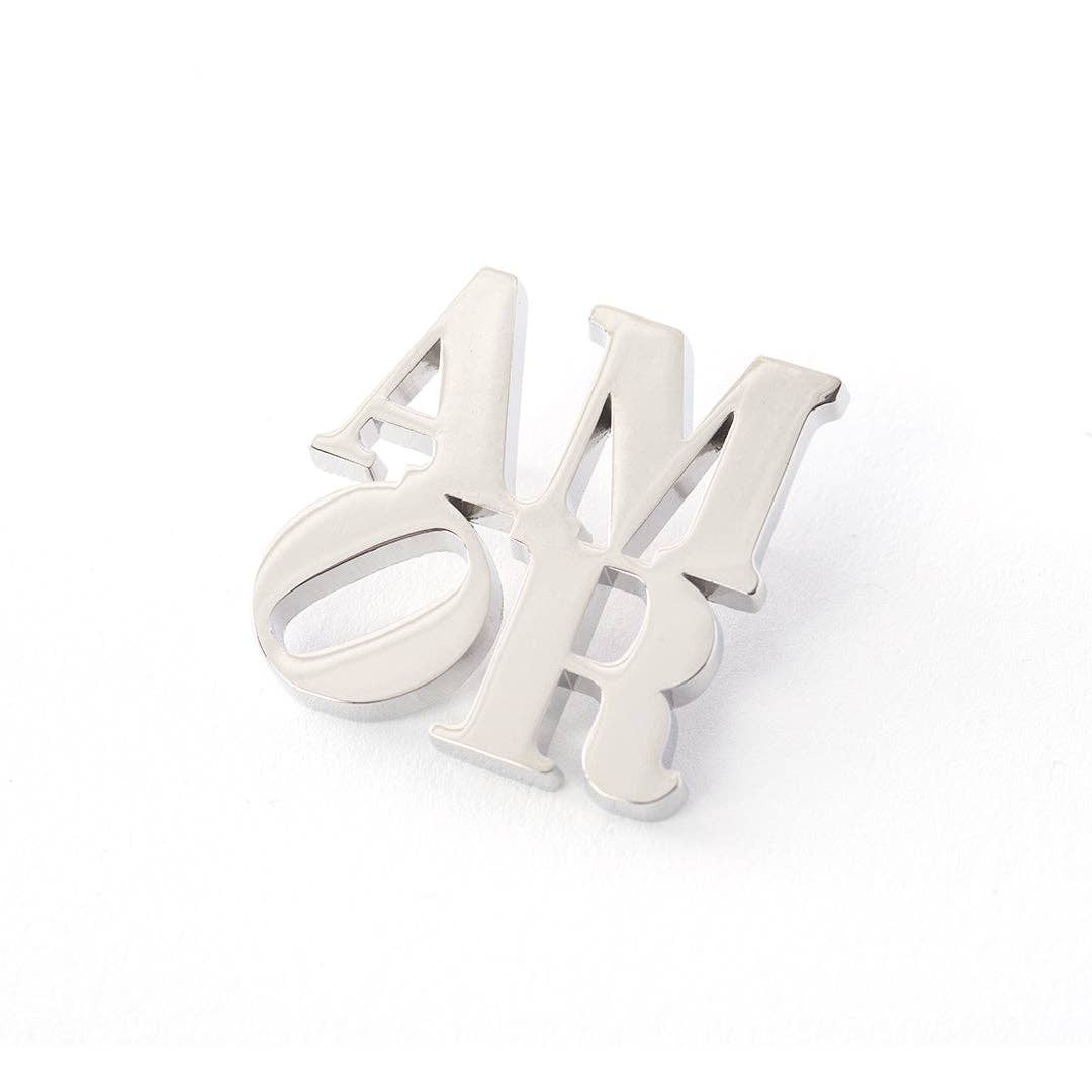 Officially licensed Robert Indiana AMOR enamel pin featuring the iconic stacked lettering in a polished silver finish.