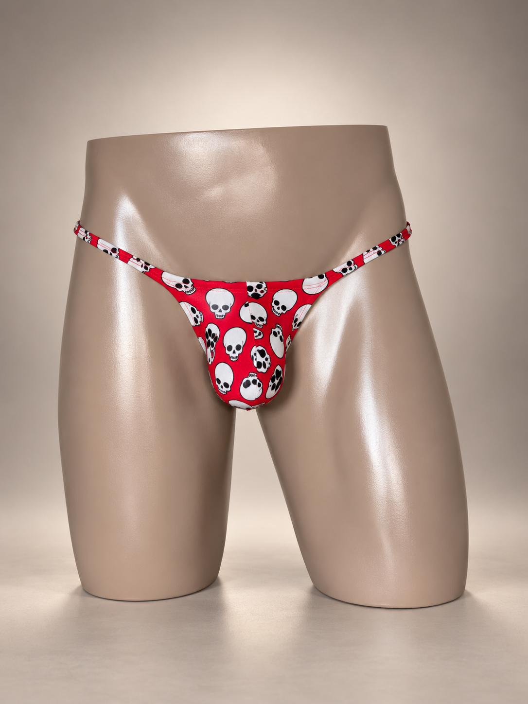 Front view of Skull Candy Muscle Thong featuring scattered white skulls with black details on red, men's Muscle thong by PapiMalo Gear.