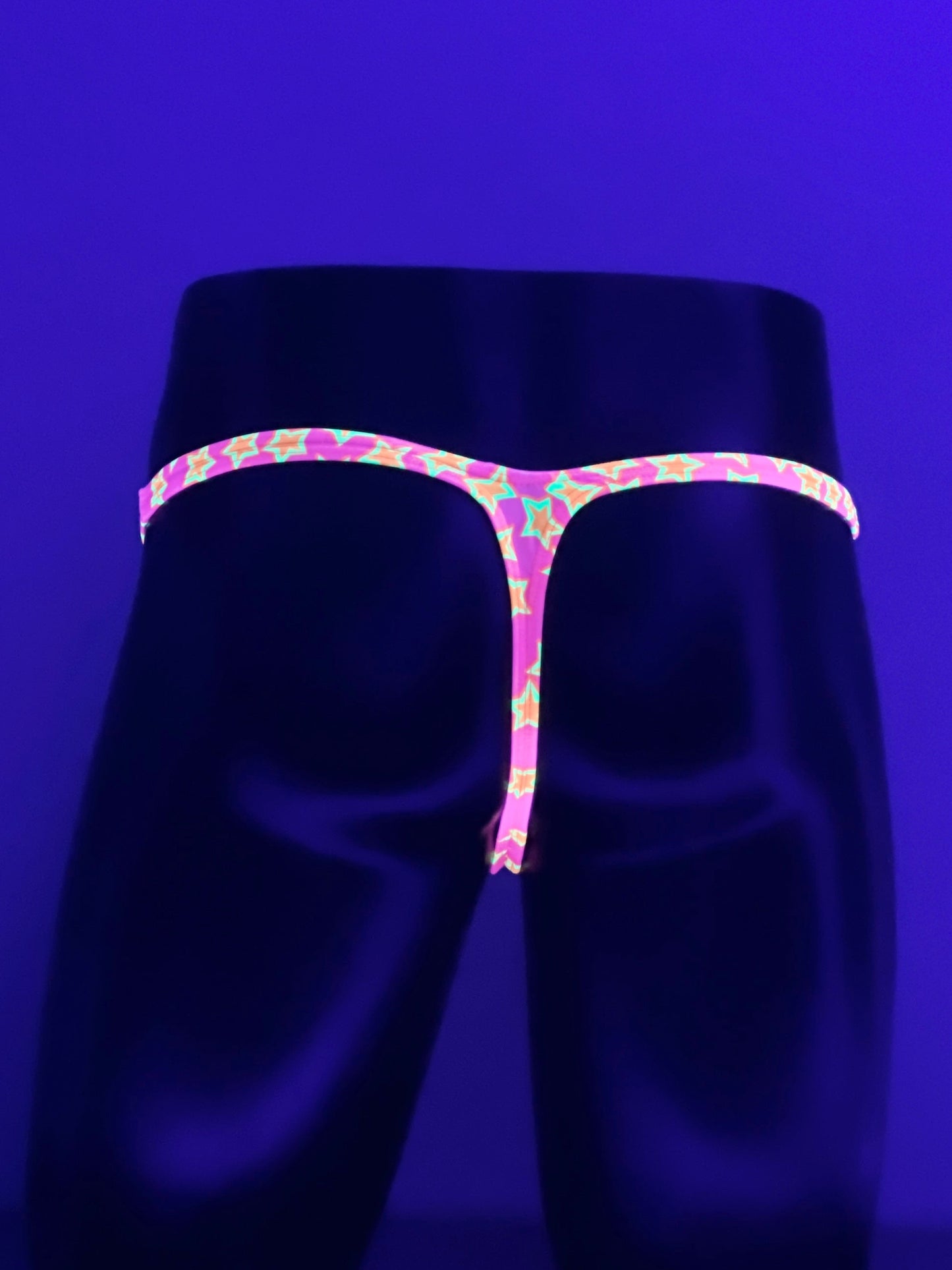 Rear View of Star Power pink star-print men’s Muscle thong glowing under UV blacklight