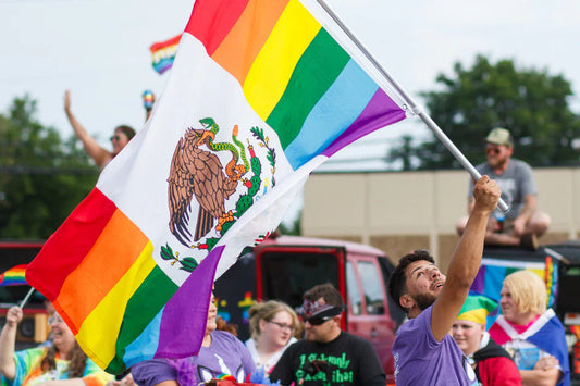 People holding a Mexican Pride outdoor flag combining rainbow pride colors with Mexican coat of arms
