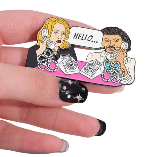 Funny enamel pin featuring parody retro phone conversation inspired by iconic “Hello” pop culture references held by a hand