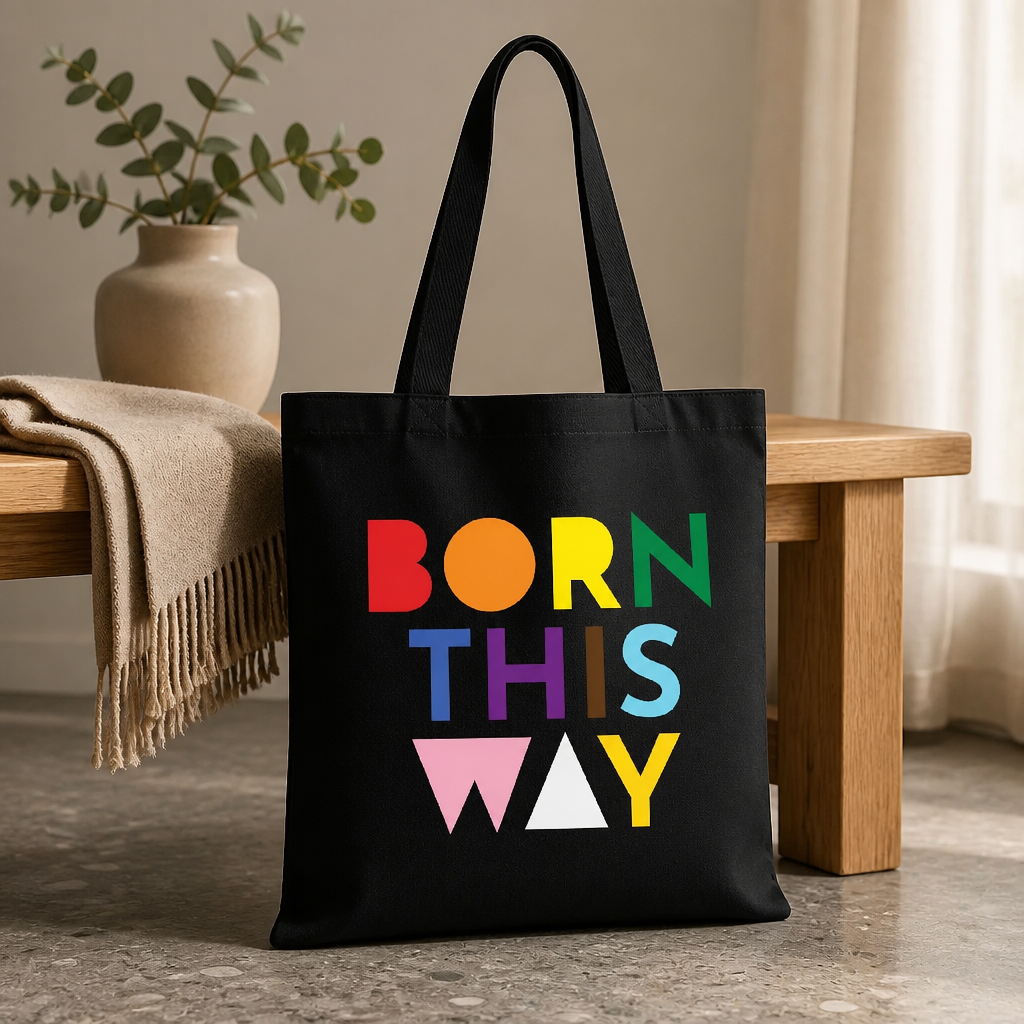 Black Born This Way Pride tote bag with colorful typography design on the floor next to a table