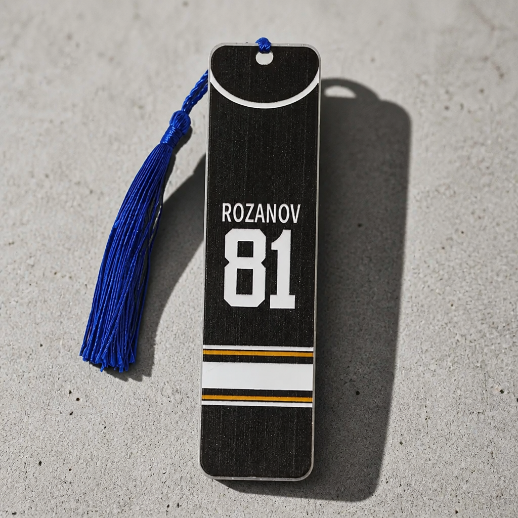 Double-sided Heated Rivalry steel bookmark featuring Hollander #24 on one side and Rozanov #81 on the reverse with blue tassel.