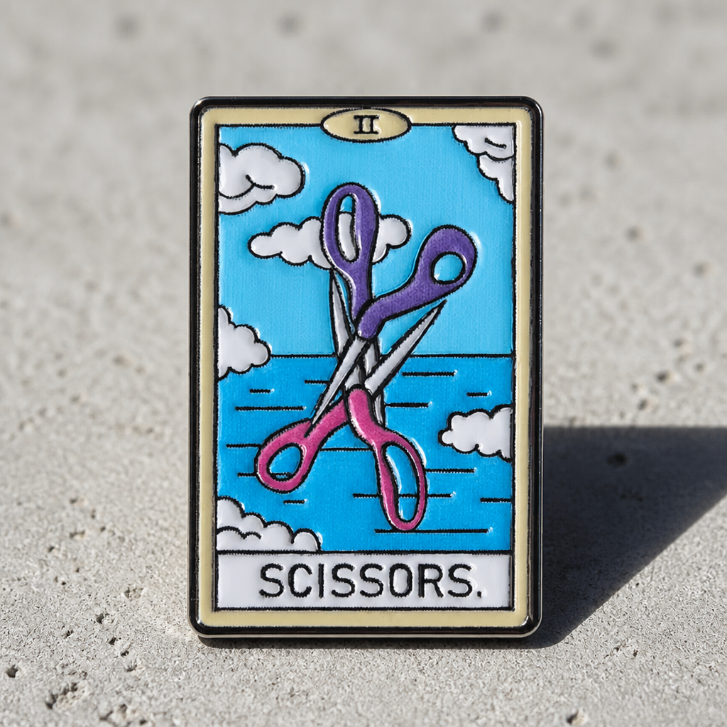 Lesbian tarot enamel pin with crossed pink and purple scissors against a blue sky displayed on a concrete surface