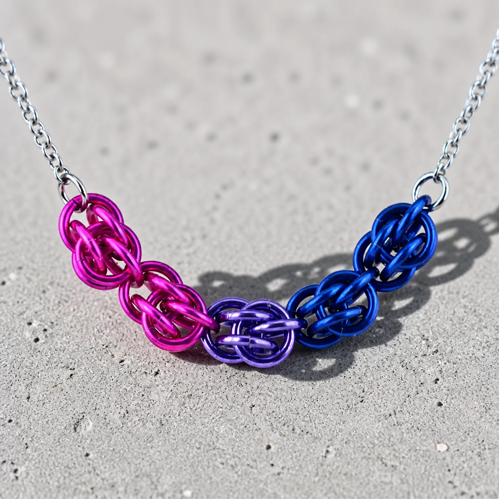 Hand-linked bisexual pride chainmail necklace featuring pink, purple, and blue aluminum rings on an adjustable stainless steel chain on a concrete surface