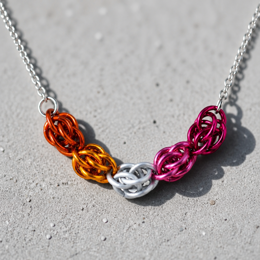 Hand-linked lesbian pride chainmail necklace featuring orange, white, pink, and magenta aluminum rings on an adjustable stainless steel chain on a concrete surface