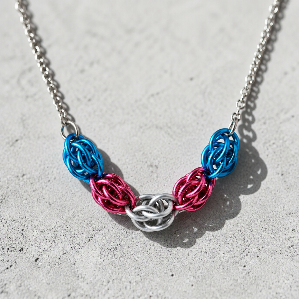 Hand-linked transgender pride chainmail necklace featuring blue, pink, and white aluminum rings on an adjustable stainless steel chain on a concrete surface