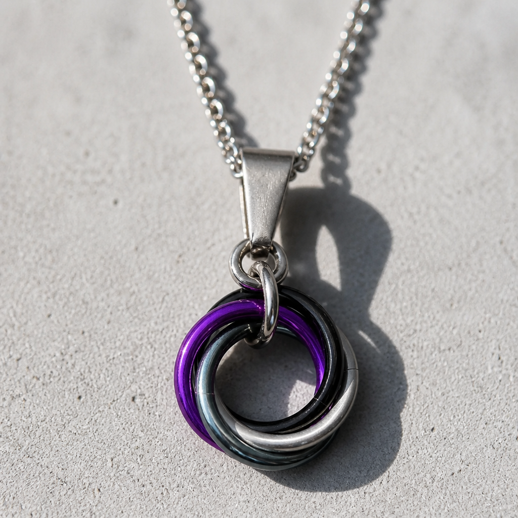 Handcrafted Asexual (ACE) Pride swirl pendant necklace featuring aluminum rings in Asexual Pride flag colors on an adjustable stainless steel chain, on a concrete surface.