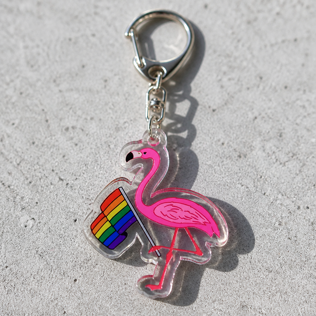 Pink flamingo acrylic keychain holding LGBTQ rainbow pride flag on a concrete surface