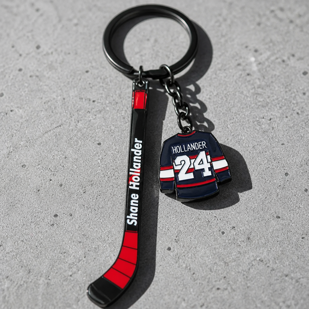 Heated Rivalry Hollander hockey stick enamel keychain with miniature jersey charm on a concrete surface