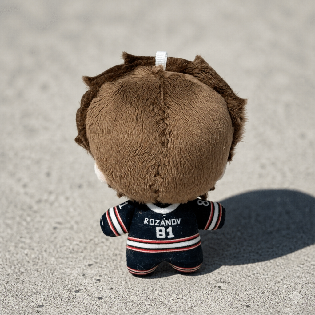 back view of Heated Rivalry Rozanov chibi-style plush keychain wearing black hockey uniform on a concrete surface
