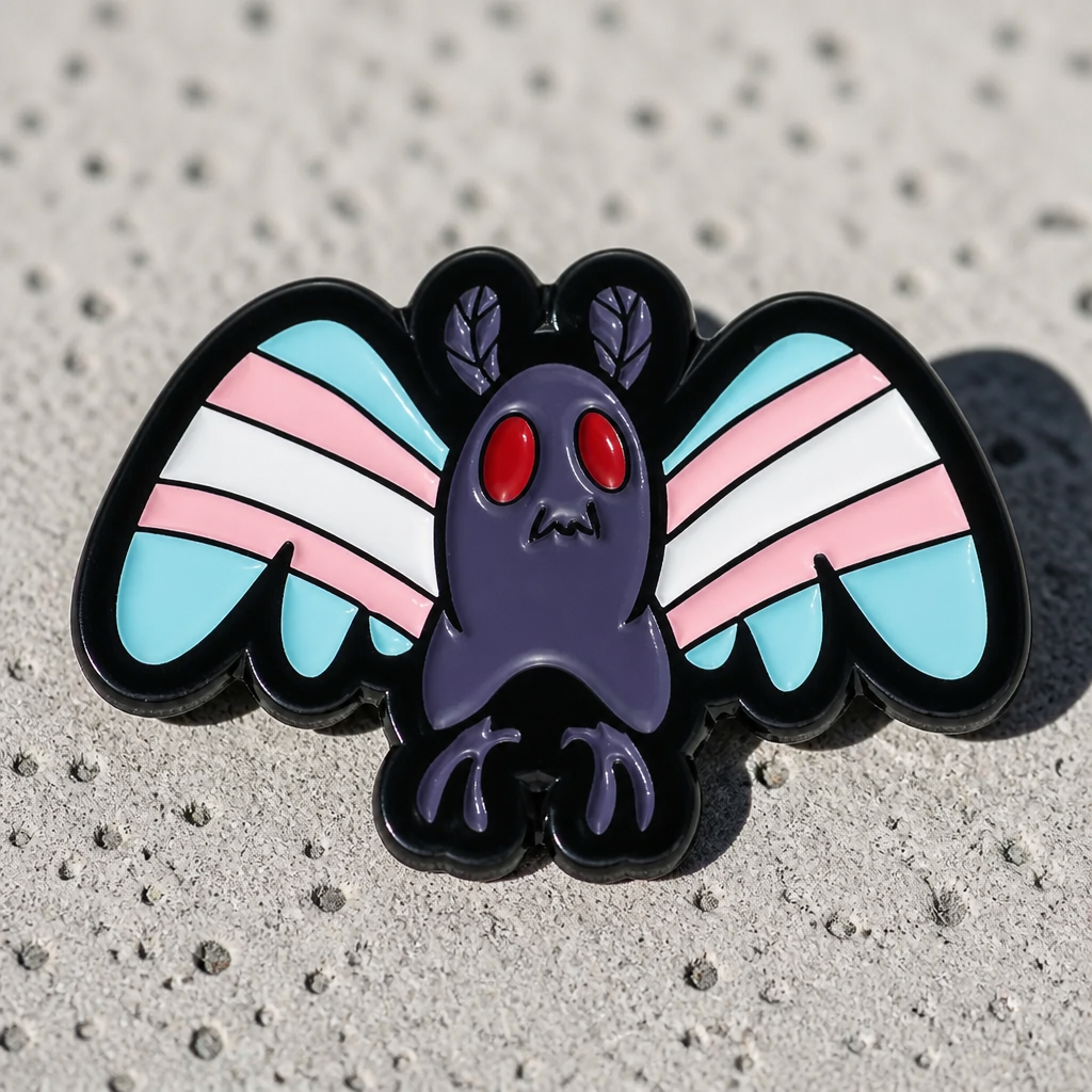 Mothman Trans Pride enamel pin featuring blue pink and white transgender Pride flag colors on a concrete surface