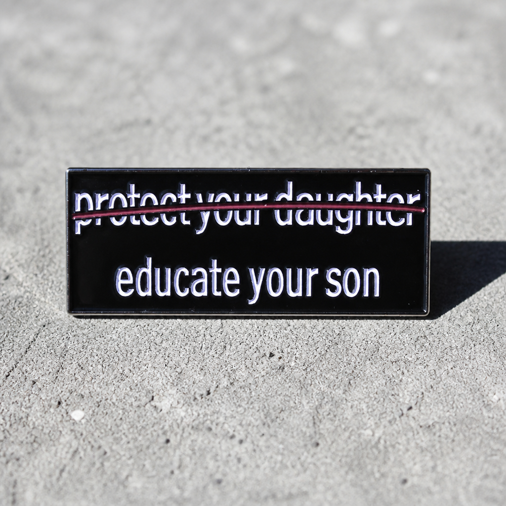 Educate Your Son enamel pin with minimalist feminist statement typography design on a concrete surface