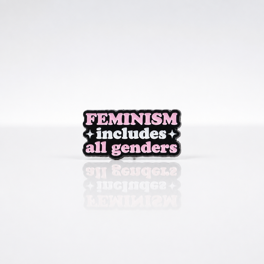 Pink and black enamel pin reading “Feminism Includes All Genders”