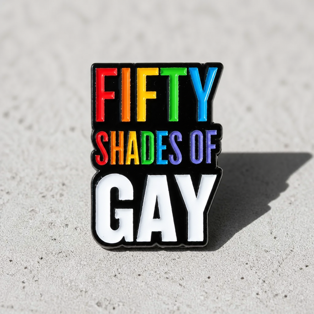 Rainbow enamel pin reading “Fifty Shades of Gay” on a concrete surface
