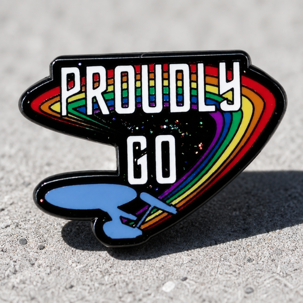Proudly Go rainbow enamel pin with glittery sci-fi inspired Pride artwork on a concrete surface