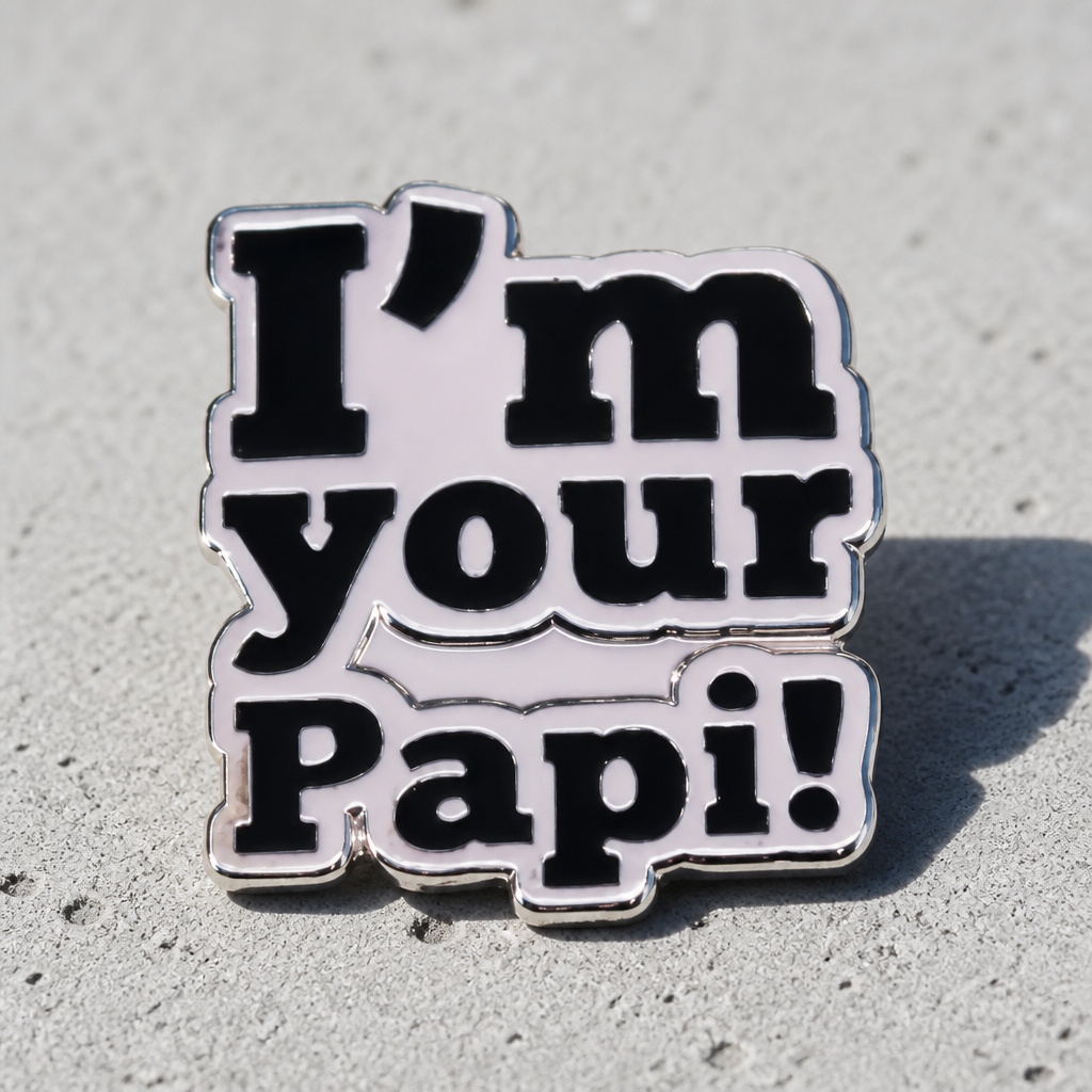 Silver enamel pin reading “I’m Your Papi!” on a concrete background