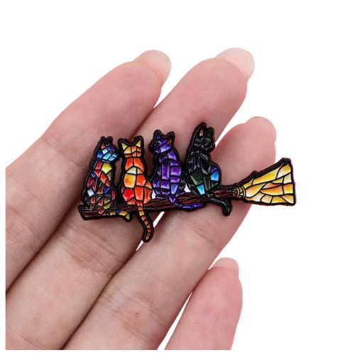 a hand holding a Colorful stained glass style enamel pin featuring cats sitting on a broomstick
