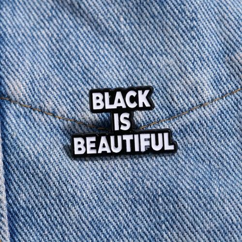 Black-and-white enamel pin reading “Black Is Beautiful” on a denim background
