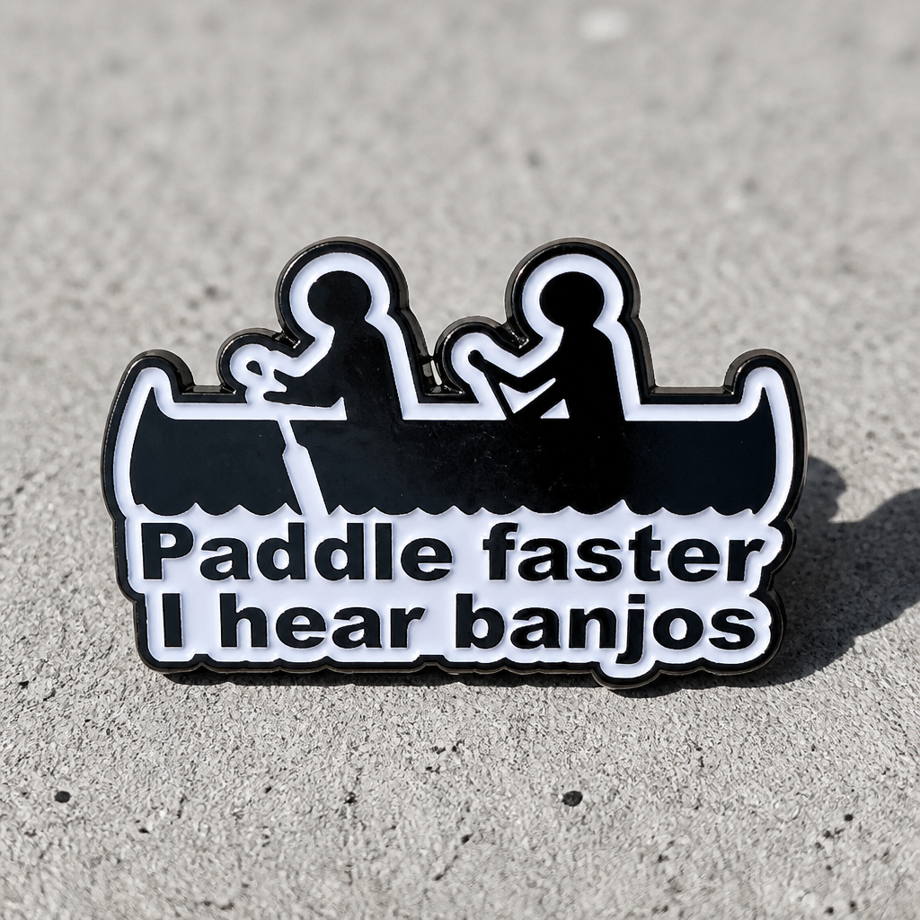 Funny enamel pin featuring two people in a canoe with Paddle Faster I Hear Banjos text on a concrete background