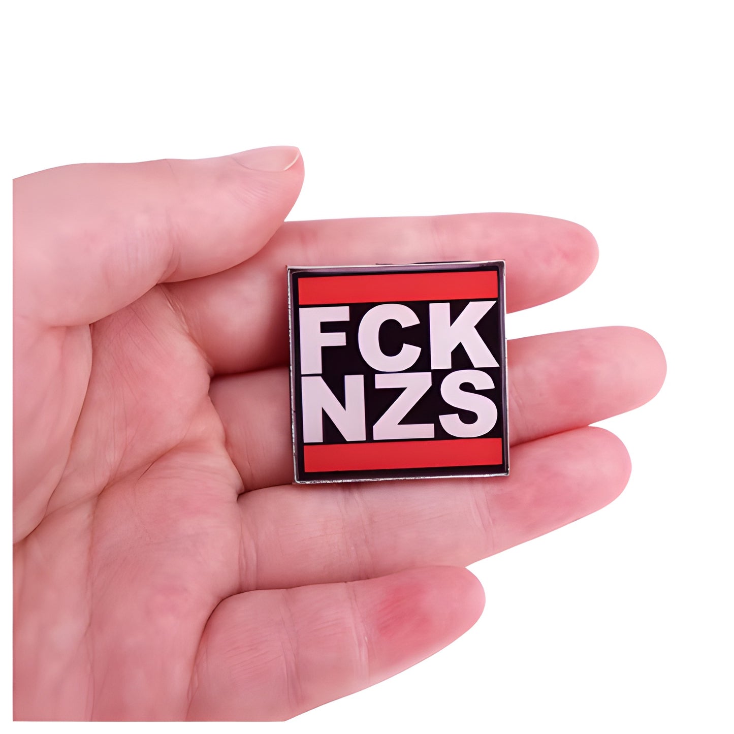 Black red and white enamel pin reading “FCK NZS” held in a hand