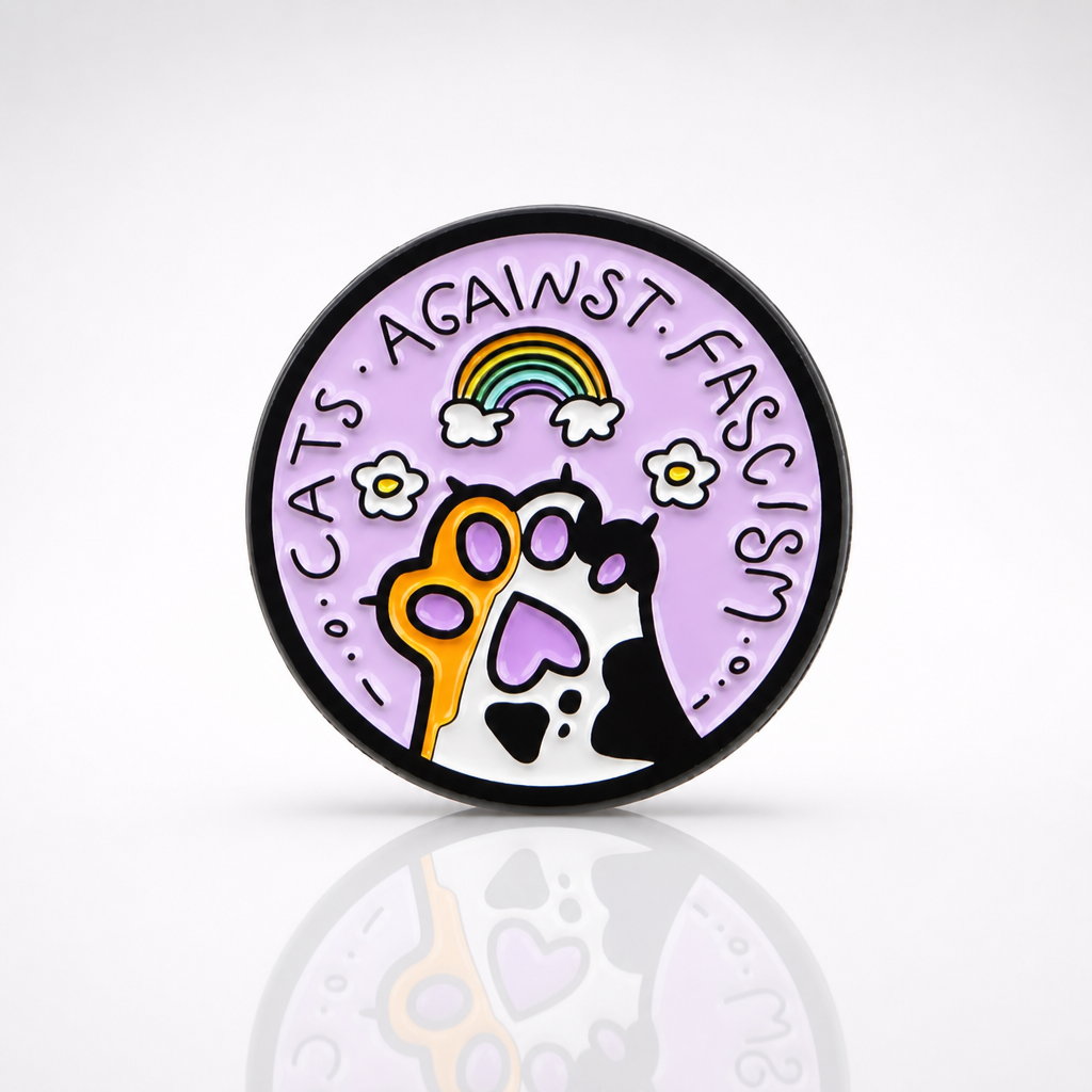 Pastel enamel pin reading “Cats Against Fascism” with rainbow and cat paw artwork