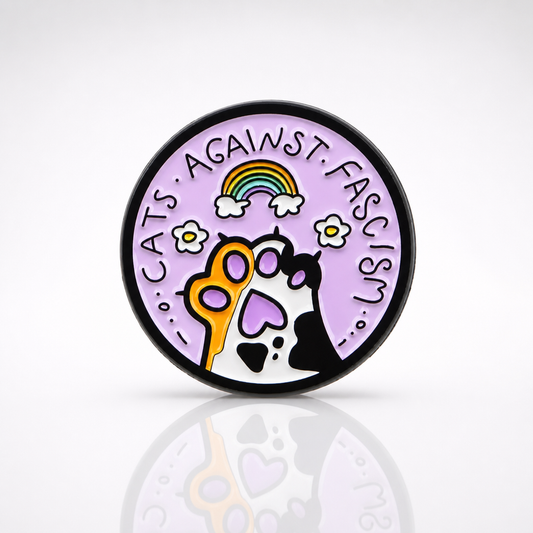 Pastel enamel pin reading “Cats Against Fascism” with rainbow and cat paw artwork